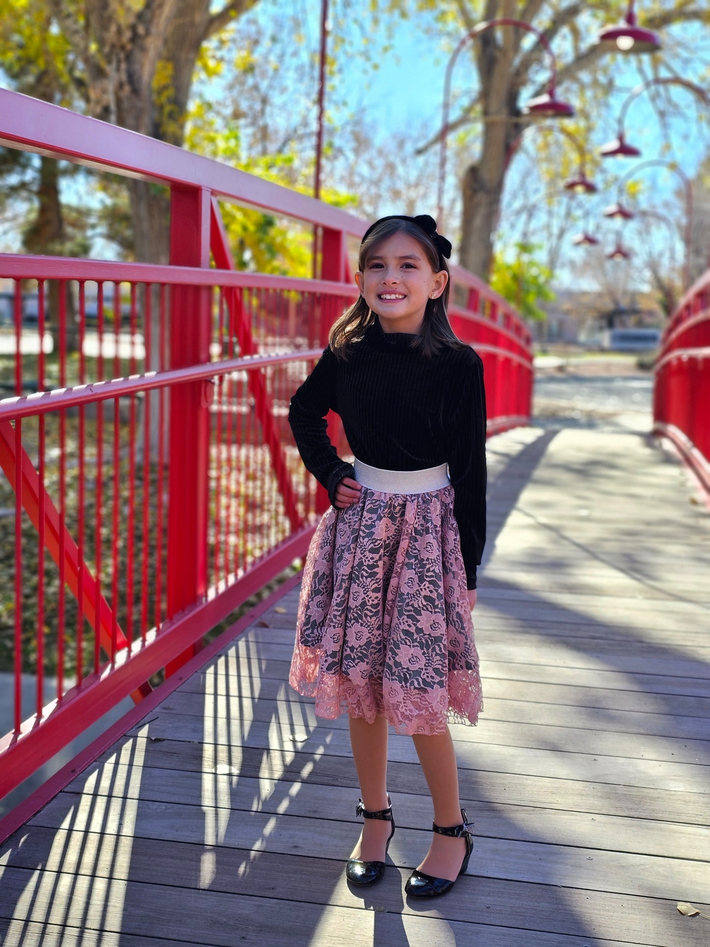 Girl standing on a bridge with a black sweater and a pink enchanted overlay skirt