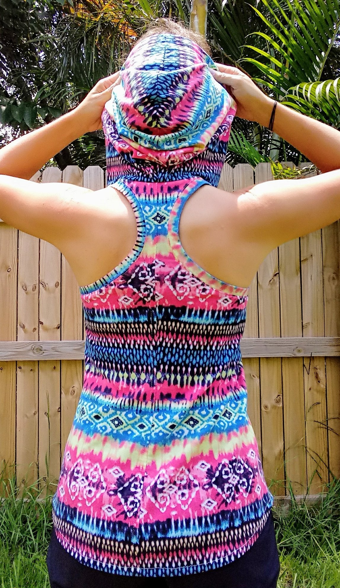 Back view of a woman wearing the Althea Racerback Tank Top with the hood up. The tank is made from a knit fabric with a pink, blue, and purple geometric pattern.