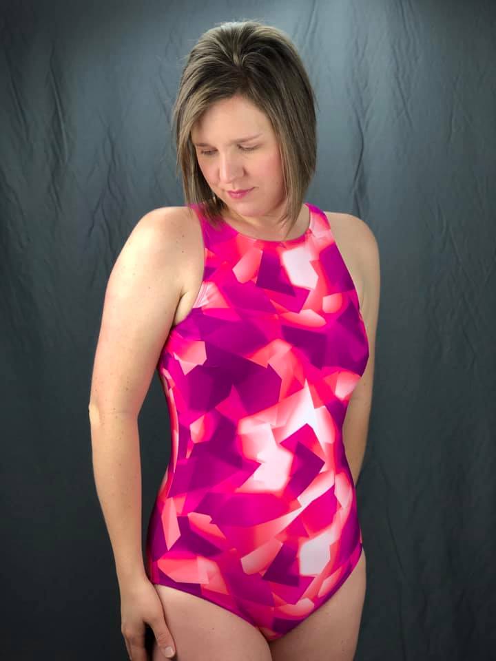 Front view of Amelia one-piece swimsuit made from a pink, purple, and white geometric fabric and high neck option.