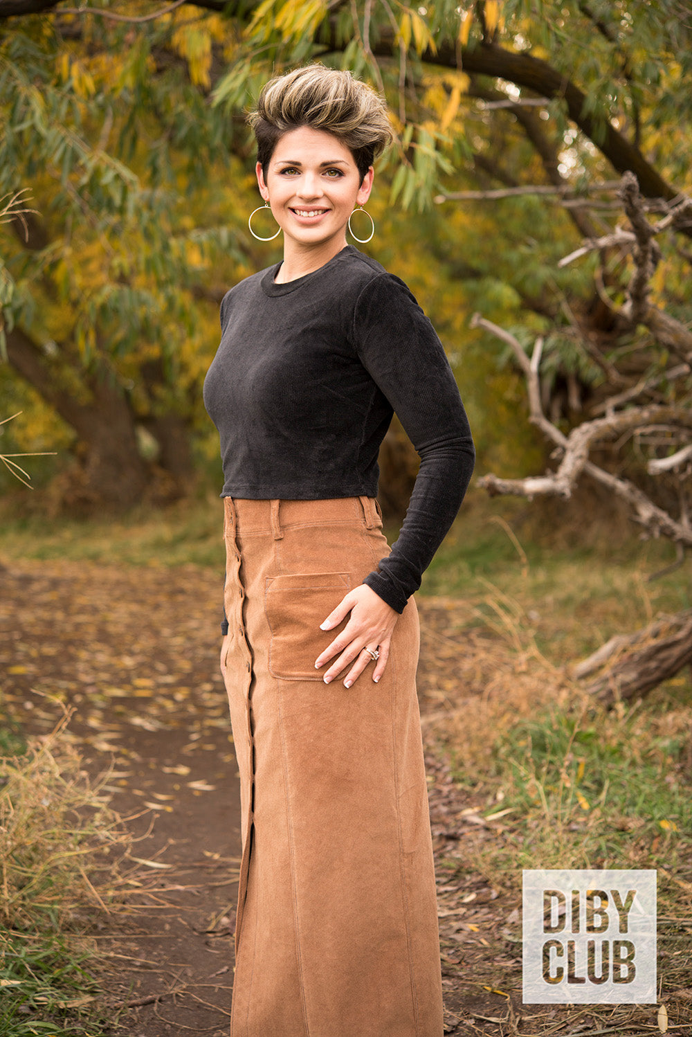 Photo of woman standing on a trail wearing a black long sleeve velvety shirt with a brown corduroy maxi-length DIBY Club Anna Button-Up Skirt