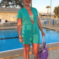A woman at a pool wearing a short sleeved DIBY Club Gabriela with a shorts option as a swim cover up. The Gabriela is made with a teal terry fabric.