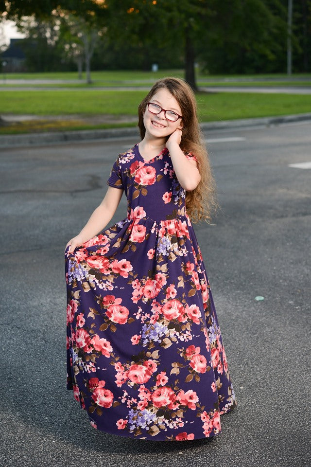 A young girl wears a floral, short sleeve, maxi-length Samantha Gathered Dress. 