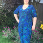 Plus size Stevie jumpsuit with elbow sleeves, slat pockets, and wide leg. Fabric material is a green floral print on blue. 